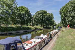 A narrow canal with boats docked along the side, surrounded by trees and grassy banks. - 1 Pines Farm Cottages (Tadcaster)