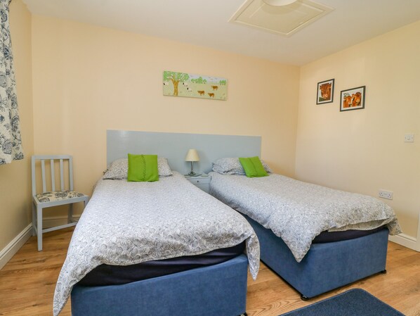 A bedroom with two beds, a nightstand, a chair, and a painting on the wall. - 1 Pines Farm Cottages (Tadcaster)