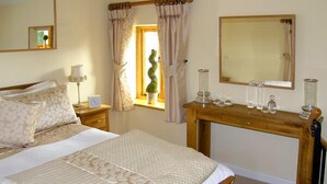 A neatly arranged bedroom with a bed, bedside tables, a wooden desk, and a mirror.