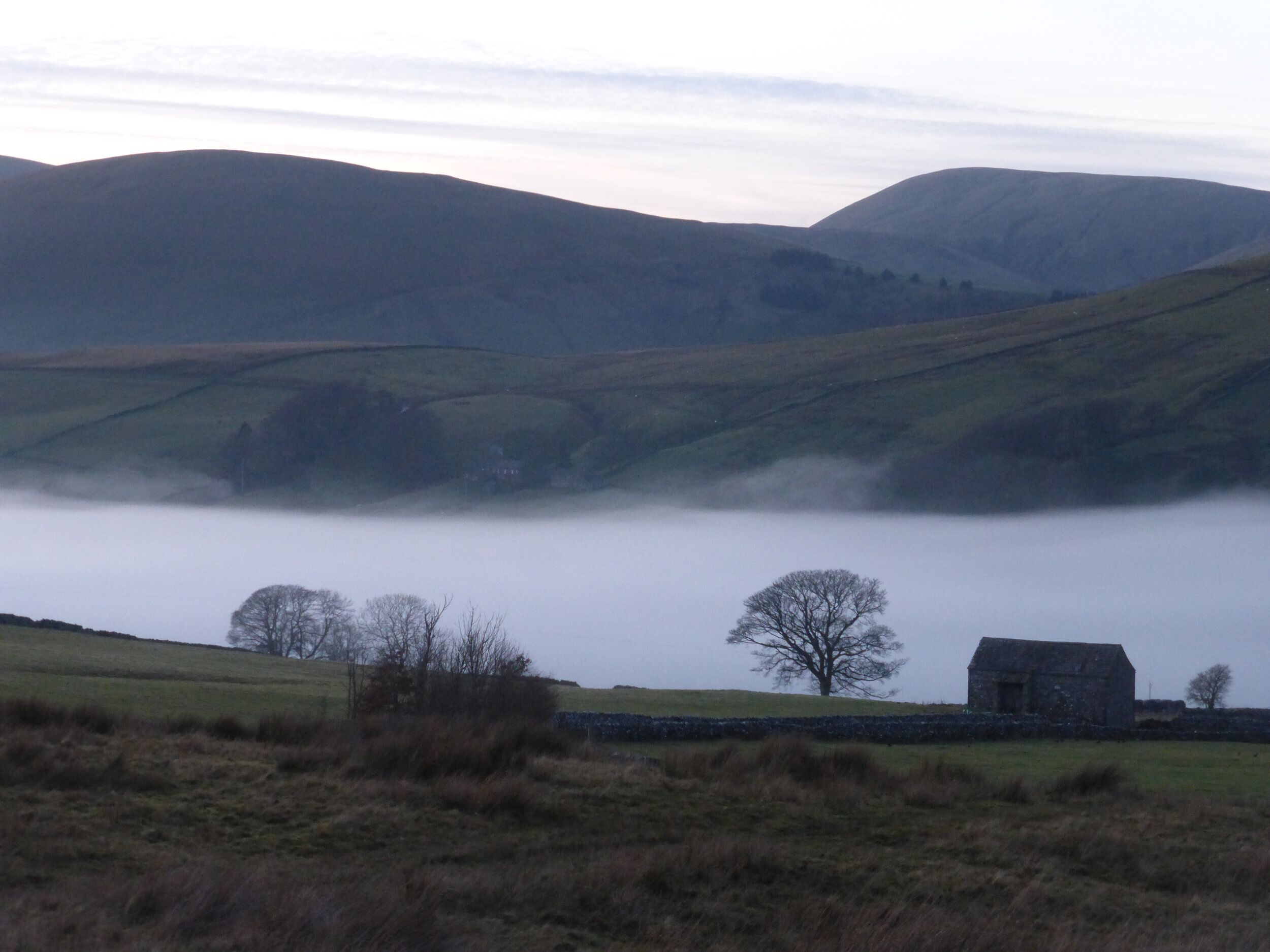 A rural landscape with rolling hills, a stone wall, and a solitary building.