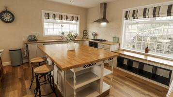 A kitchen with a wooden island, bar stools, a clock, and a window with a view of a garden.