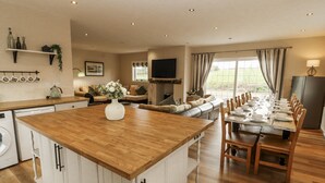 A spacious kitchen with a central island, a dining area with a long table, and a cozy living area with a sofa and TV. - White Gables (Workington)
