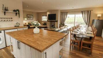 A spacious kitchen with a central island, a dining area with a long table, and a cozy living area with a sofa and TV.