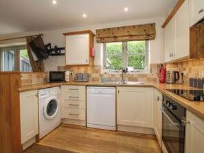 A compact kitchen with a washing machine, dishwasher, microwave, and a built-in oven. - The Turnip House (Craven Arms)