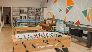 A room with a foosball table, a pool table, and a foosball table with 'Strikeworth' branding. There is a bookshelf filled with books and a colorful geometric wall design. - The Turnip House (Craven Arms)