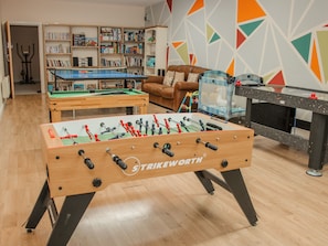 A room with a foosball table, a pool table, and a foosball table with 'Strikeworth' branding. There is a bookshelf filled with books and a colorful geometric wall design. - The Turnip House (Craven Arms)