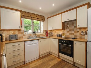 A kitchen with white cabinets, a dishwasher, an oven, a sink, and a window with a view of greenery outside. - The Turnip House (Craven Arms)