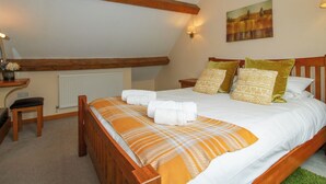 A bedroom with a wooden bed, a radiator, a desk with a chair, and a painting on the wall. - The Turnip House (Craven Arms)