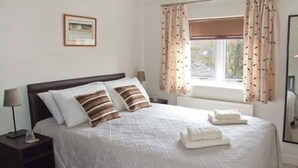 A neatly made bed with a quilted white duvet, two pillows, and two folded towels on the side. - Hour Cottage (Cheltenham)