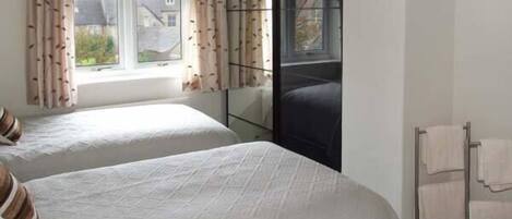 A bedroom with two beds, a window with curtains, a mirror, and a towel rack.