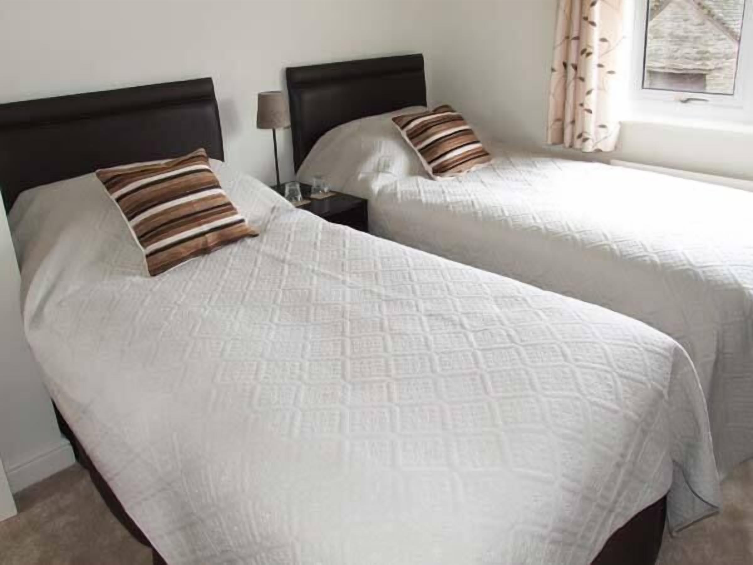 Two single beds with headboards, a bedside table with a lamp, and a window with curtains.