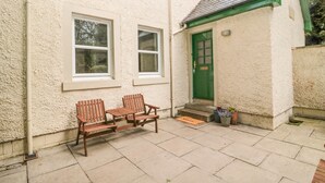 A house with a green door, two windows, and a small porch with two wooden benches. - Groom's Cottage (Duns)