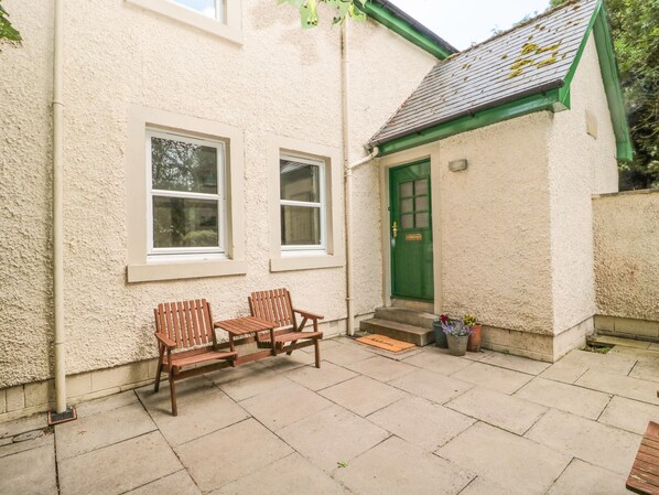 Une maison avec une porte verte, deux fenêtres et un petit porche doté de deux bancs en bois.