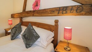 Ein Bett mit Holzkopfteil, zwei Kissen, ein Nachttisch mit Lampe und eine Wand mit Holzbalken und einer rosa Blumendekoration.
