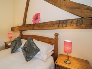 A wooden bed with a headboard, two pillows, a nightstand with a lamp, and a wall with a wooden beam and a pink flower decoration. - Bwthyn Y Wennol (Abergele)