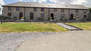 Ein Steinhaus mit mehreren Fenstern und Eingängen, Sitzgelegenheiten im Freien und einem Kiesweg.