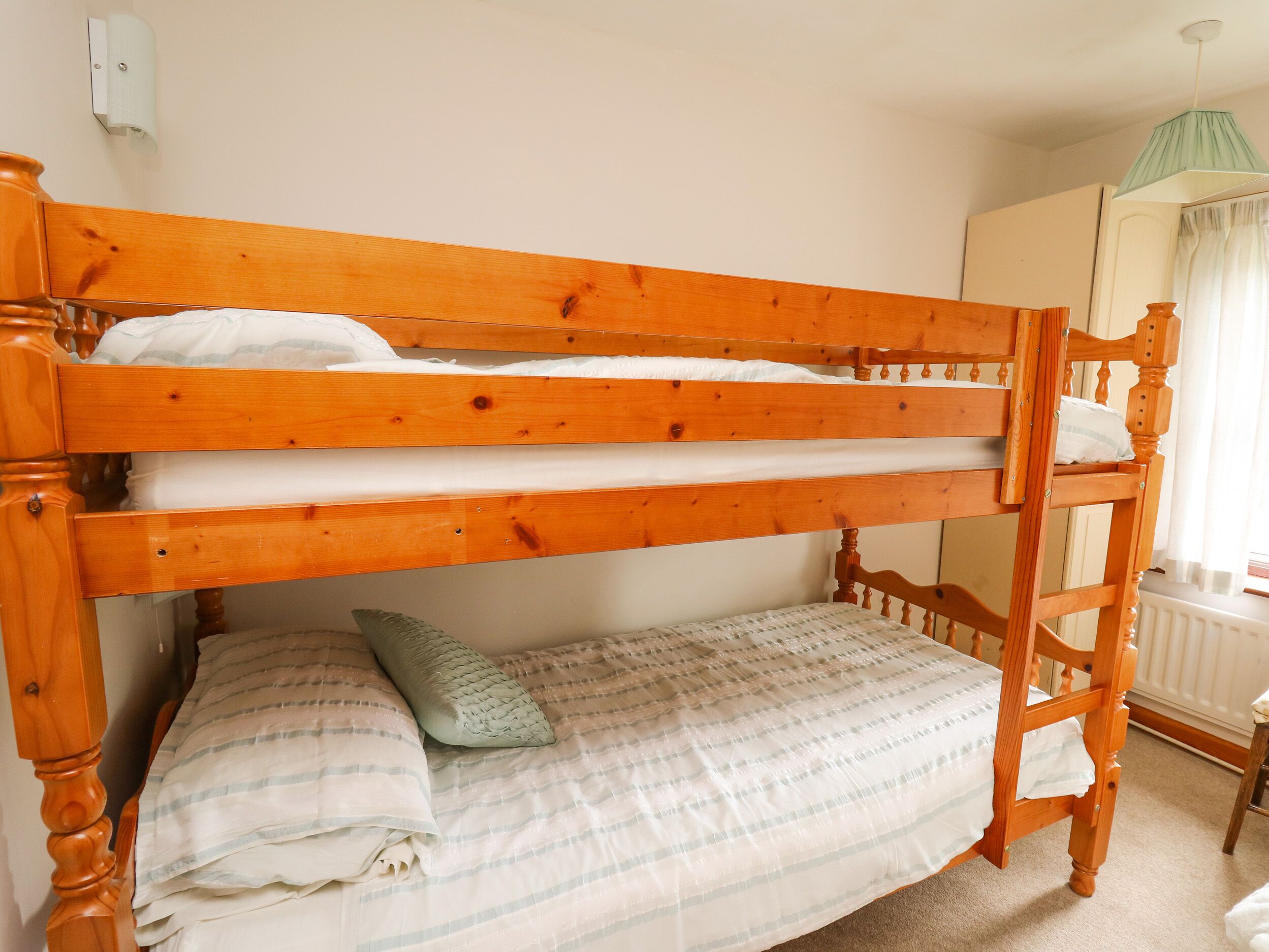 Cama litera de dos niveles, mesita de noche, lámpara y radiador.