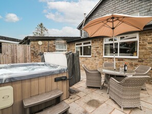 A hot tub, wicker chairs, and a table with a bottle and glass in a backyard with stone walls and a wooden fence. - Holly Farm Cottage (Llandrindod Wells)