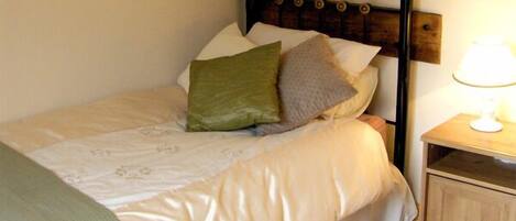 A bedroom with a bed, pillows, a nightstand, and a lamp.