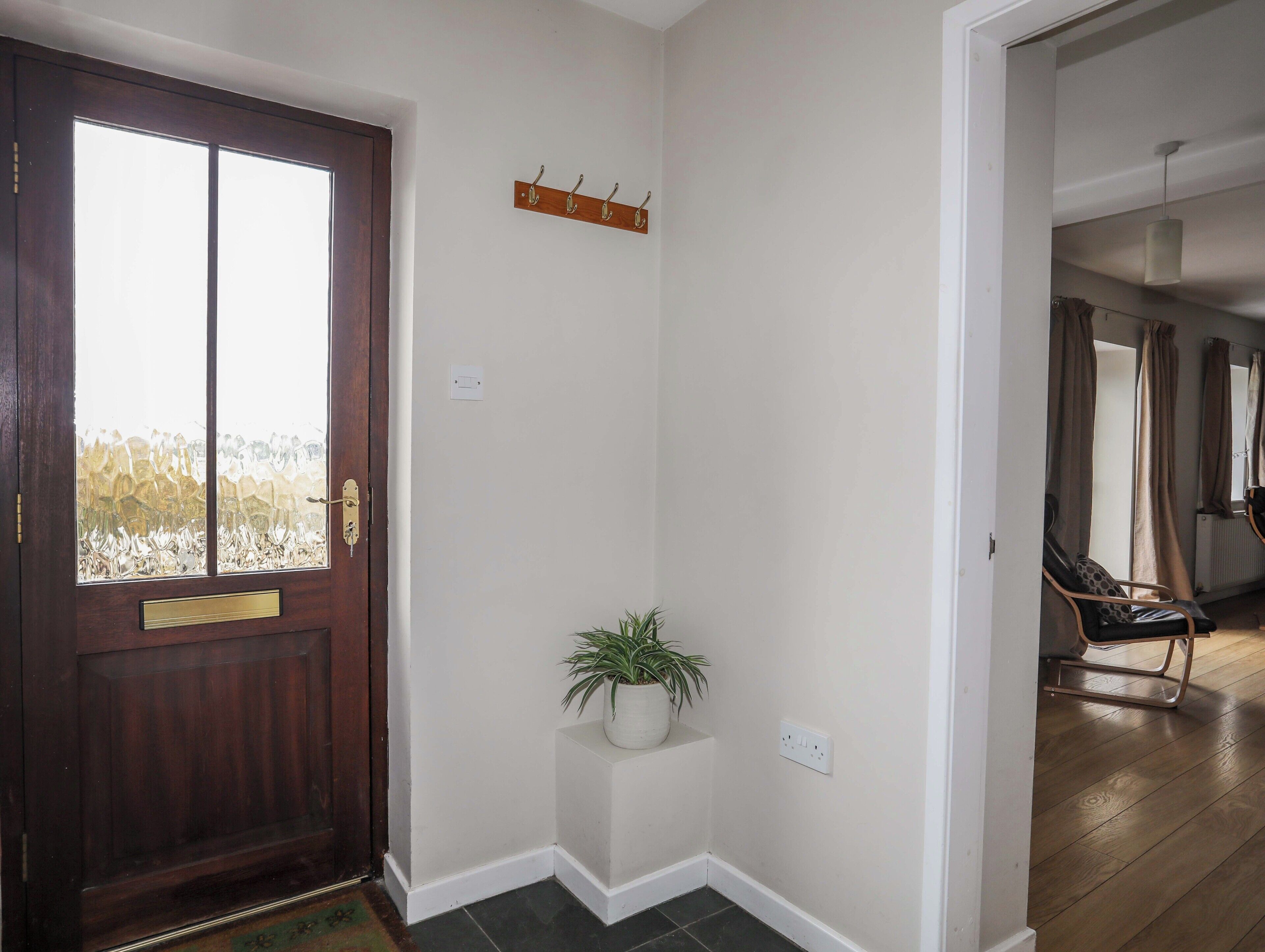 Un pasillo con una puerta de madera, una planta en maceta, un perchero y una silla en una habitación.