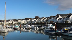 A marina with various boats docked, surrounded by residential houses. - Penrallt Cottage (Y Felinheli)
