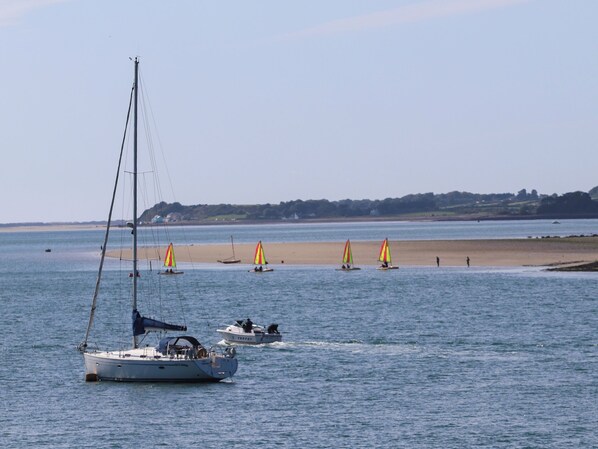 A calm sea with several sailboats and a yacht. There is a sandy beach in the background with a few people walking. - Penrallt Cottage (Y Felinheli)
