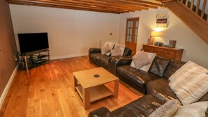 A living room with a wooden floor, leather sofa, a coffee table, a TV on a stand, and a staircase. - Cefn-yr-efail (Garndolbenmaen)