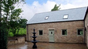 A stone building with a tiled courtyard, a fountain, and a door. - Alveton (Stoke-on-Trent)