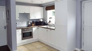 A compact kitchen with white cabinets, a built-in oven, and a microwave. - Alveton (Stoke-on-Trent)