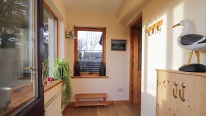 A hallway with a wooden bench, a wooden cabinet with hooks, a framed picture on the wall, and a window with a view of trees and buildings.
