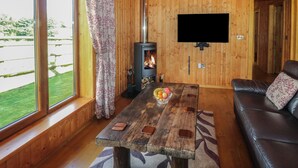 Interior acolhedor de cabana com decoração em madeira, lareira, TV de tela plana na parede e sofá de couro.