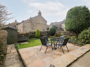 A stone patio with a table and chairs, a stone wall, and a stone building in the background.