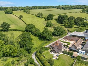 An aerial view of a rural property with a large house, barns, and expansive green fields. - The Olde Cowshed (Craven Arms)