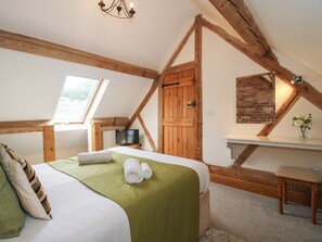 A bedroom with a bed, a television, a wooden door, a window, and a small table with a vase.