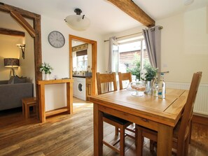 A wooden dining table with chairs, a kitchen area with a washing machine, and a living room with a sofa and lamp. - The Olde Cowshed (Craven Arms)