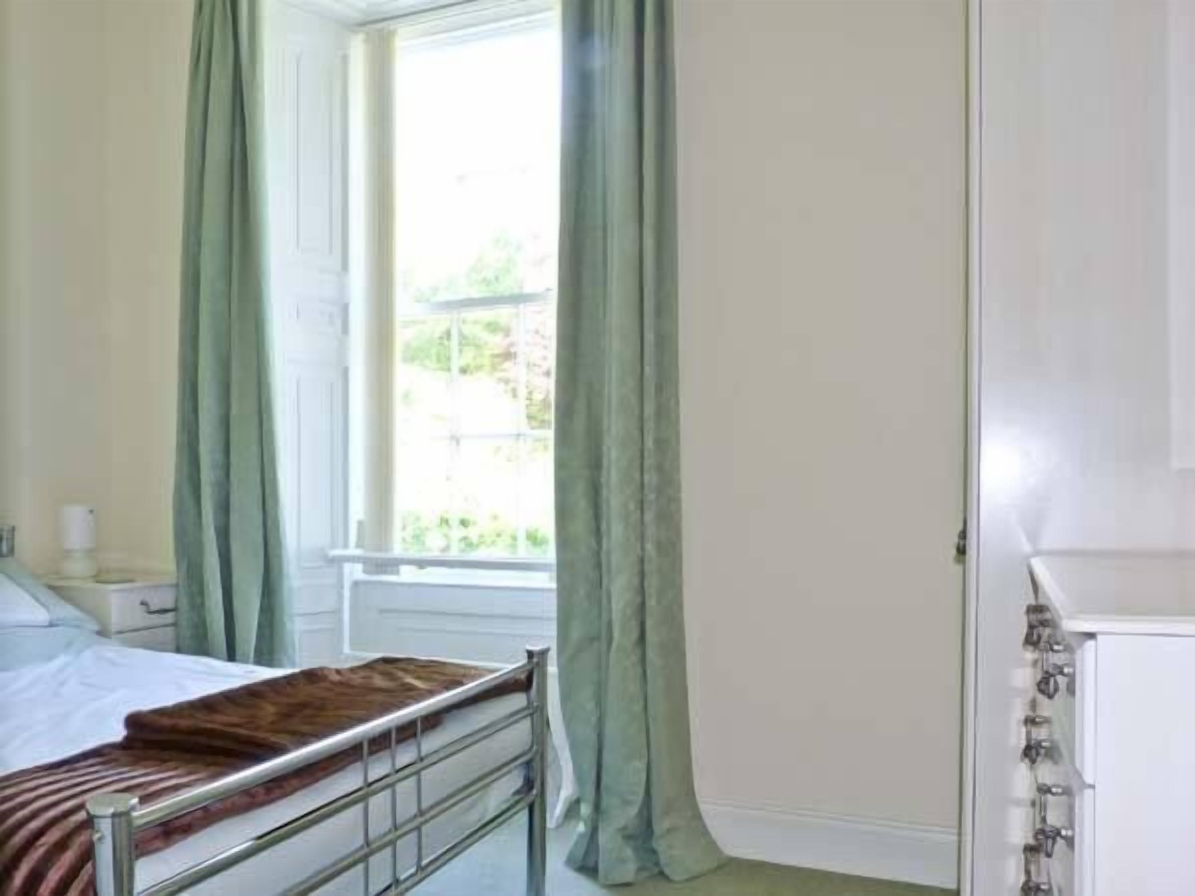 A room with a bed, a window with curtains, and a white cabinet.