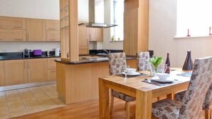 A modern kitchen with wooden cabinets, a central island, and a dining area with floral chairs. - 2 Cark House (Grange-over-Sands)