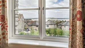 Ett fönster med utsikt över ett bostadsområde, byggnader i sten och ett avlägset landskap.