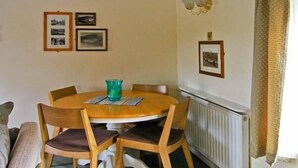 A dining area with a round wooden table, four wooden chairs, and a green glass vase.