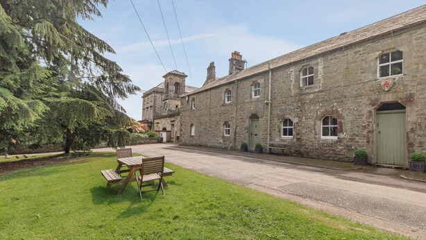 A stone building with a green door, a bench, and a tree in the foreground. - Reiver's Rest (Hexham)