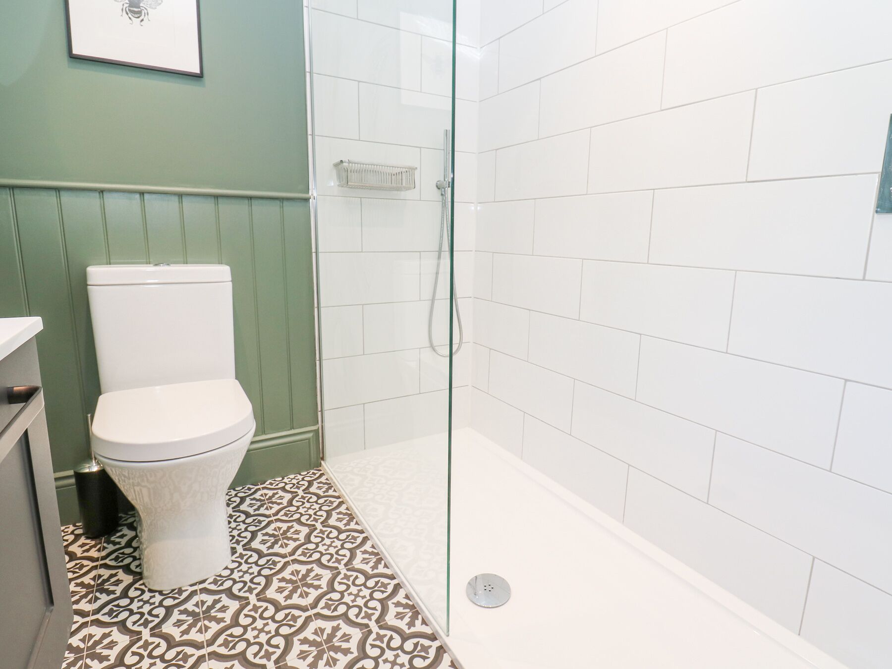 Un baño con inodoro, ducha y baldosas de suelo con diseño.