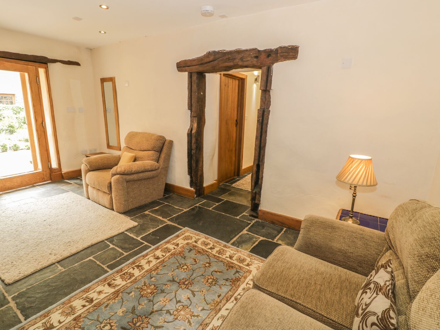 A cozy living room with a stone floor, a patterned rug, a wooden archway, and a lamp.