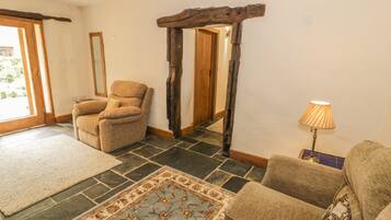 A cozy living room with a stone floor, a patterned rug, a wooden archway, and a lamp.