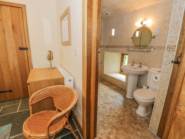 Un baño con puerta de madera, una silla de mimbre, un espejo, un lavabo y un inodoro.