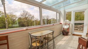 A conservatory with a table and chairs, a wicker basket, and a bench. - Gun End Cottage (Macclesfield)