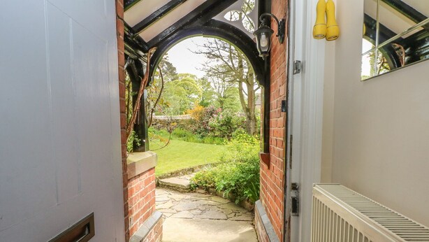 A narrow entrance with a brick wall, a white door, and a small garden visible through an archway. - Gun End Cottage (Macclesfield)