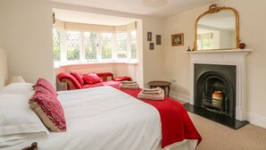 A bedroom with a large bed, a fireplace, a window with a view, and a mirror on the wall. - Gun End Cottage (Macclesfield)
