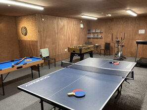 Enjoy games, fitness, and relaxation in this room featuring a ping pong table, foosball table, dartboard, bookshelf, and treadmill.