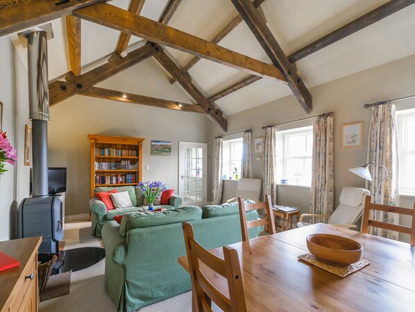 A cozy living room with a fireplace, green sofa, wooden dining table, and a bookshelf. - The Byre at High Watch (Bishop Auckland)