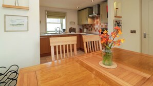 Moderni keittiö, jossa on puiset kaapit, ruokapöytä tuoleineen sekä maljakko kukkineen pöydällä.